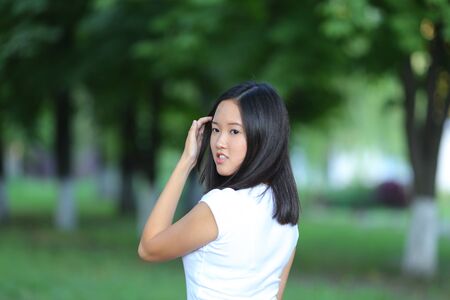 Girl female teenager with black hair in a bob white east Asian woman green park with a backpack background. Lady holds, dials, push your finger, smiling, looking into the camera, talking on the phone happy portrait.の写真素材