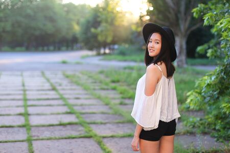 female nature keeps his hat summer sun sunset looks pleased. azitka woman black hair white shirt black shorts dancing around the trees looking at the camera. portrait. spinningの写真素材