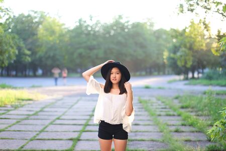 female nature keeps his hat summer sun sunset looks pleased. azitka woman black hair white shirt black shorts dancing around the trees looking at the camera. portrait. spinningの写真素材