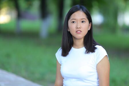 Girl female teenager with black hair in a bob white east Asian woman green park background. Lady holding plate and presses a finger, smiling, looking into the camera.の写真素材