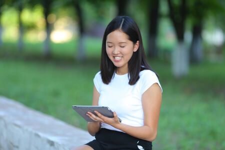 Girl female teenager with black hair in a bob white east Asian woman green park background. Lady holding plate and presses a finger, smiling, looking into the camera.の写真素材