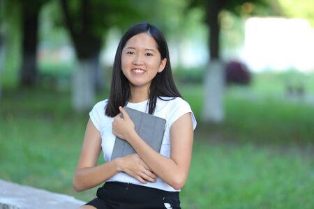 Girl female teenager with black hair in a bob white east Asian woman green park background. Lady holding plate and presses a finger, smiling, looking into the camera.の写真素材