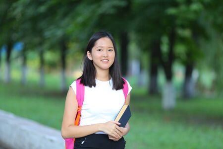 Girl female teenager with black hair in a bob white east Asian woman green park with a backpack background. Lady holds, dials, push your finger, smiling, looking into the camera, talking on the phone happy portrait.の写真素材
