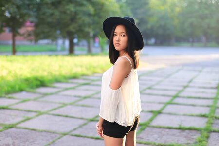 female hat nature summer sun sunset looks pleased. azitka woman black hair white shirt black shorts dancing around the trees looking at the camera. portrait.の写真素材