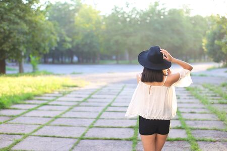female nature keeps his hat summer sun sunset looks pleased. azitka woman black hair white shirt black shorts dancing around the trees looking at the camera. portrait. spinningの写真素材