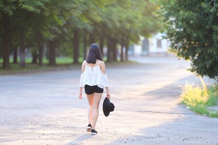 female nature keeps his hat summer sun sunset looks pleased. azitka woman black hair white shirt black shorts out trees around.の写真素材