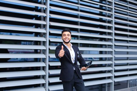 Young handsome businessman Arab Muslims is in the business center in black elegant dress on building background. Businessman man male looking waiting concept and smiling.の写真素材