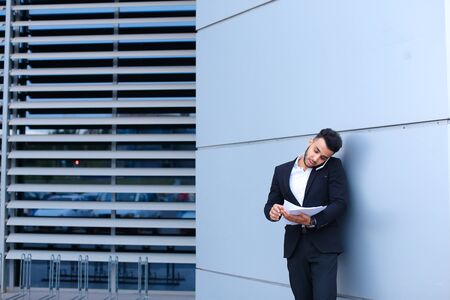 Entrepreneur man male looking at camera and smiling point hand to entrance door. Young handsome businessman arab muslims in business center wearing dressed in black elegant suit on building background.の写真素材