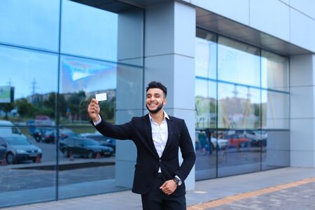 Entrepreneur looking demonstrate show card to camera. Young handsome businessman arab muslims in business center wearing dressed in black elegant suit on building background.の写真素材