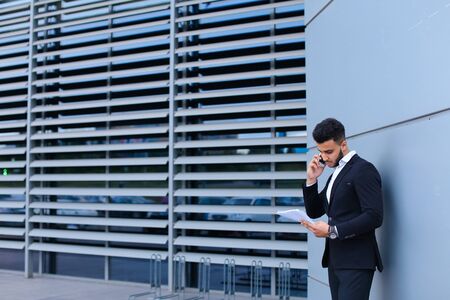 Entrepreneur man male looking at camera and smiling point hand to entrance door. Young handsome businessman arab muslims in business center wearing dressed in black elegant suit on building background.の写真素材