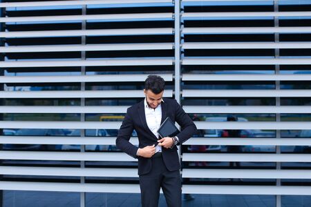 Entrepreneur uses tablet for online order shopping with debit credit card looking smiling at the camera. Young handsome businessman arab muslims in business center wearing dressed in black elegant suit on building background.の写真素材