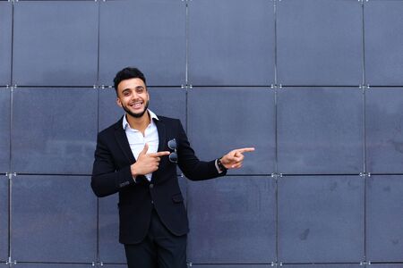 Young handsome businessman Arab Muslims is in the business center in black elegant dress on building background. Businessman man male looking at time walking goes and smiling.の写真素材