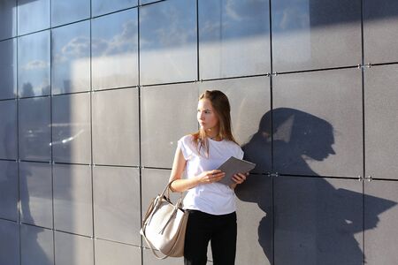 Female work, negotiating, solves problems, browsing touch looking tablet. Young beautiful business woman entrepreneur with long hair wearing suit standing near center technology sun.の写真素材