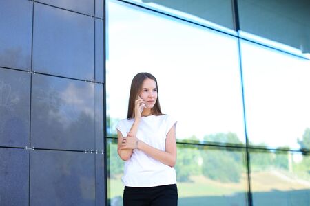 Young beautiful business woman entrepreneur with long hair wearing a suit standing near center business technology. Female work, negotiating, solves problems, dials, talking on smart phoneの写真素材