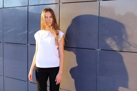 Young cute female girl student smiling, straightens hair, posing for camera and stands near modern business cente.の写真素材