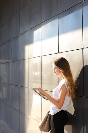 Female work, negotiating, solves problems, browsing touch looking tablet. Young beautiful business woman entrepreneur with long hair wearing suit standing near center technology sun.の写真素材