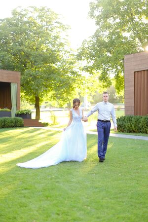 Caucasian bride walking in park with groom, wearing white amazing dress. Concept of wedding and bridal photo session in open air.の写真素材