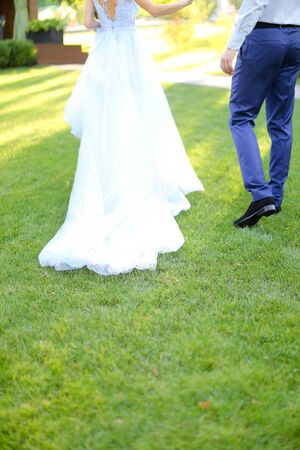 Back view of bride and groom walking in garden on green grass. Concept of wedding and bridal photo session.の写真素材
