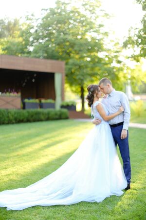 Amazing fiancee in white dress dancing in park with groom on shiny green grass. Concept of wedding and bridal photo session in open air.の写真素材