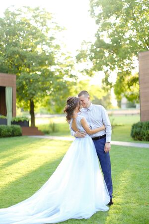 Amazing american fiancee dancing in park with groom on shiny green grass. Concept of wedding and bridal photo session in open air.の写真素材