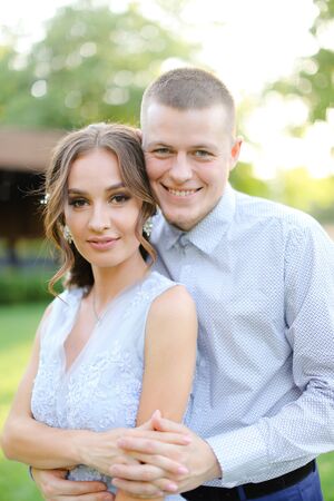 Happy groom hugging beautiful fiancee in park, sun rays. Concept of bridal couple and wedding photo session in open air.の写真素材