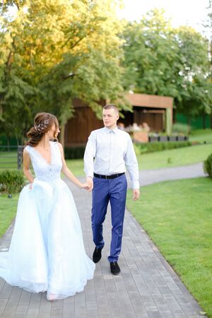 Young european fiancee walking with caucasian groom in park. Concept of happy couple and wedding photo session outside.の写真素材