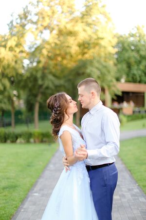 Young fiancee walking kissing with caucasian groom in park. Concept of happy couple and wedding photo session outside.の写真素材