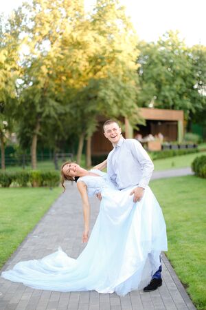 Young european fiancee dancing with groom in park and wearing white dress. Concept of wedding and bridal photo session.の写真素材