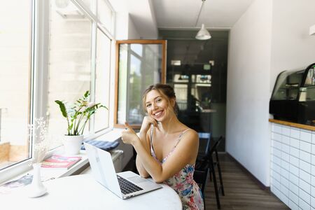Young caucasian woman showing thumbs up and sitting at cafe, surfing internet by laptop. Concept of freelance job and home business.の写真素材