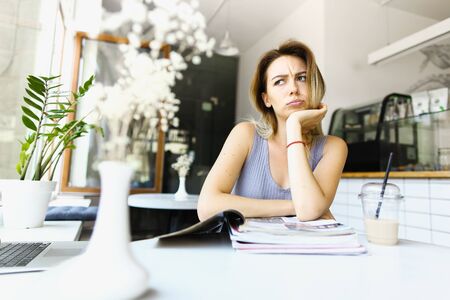 Young thoughtful woman reading magazines at cafe near laptop. Concept of taking rest and student life.の写真素材