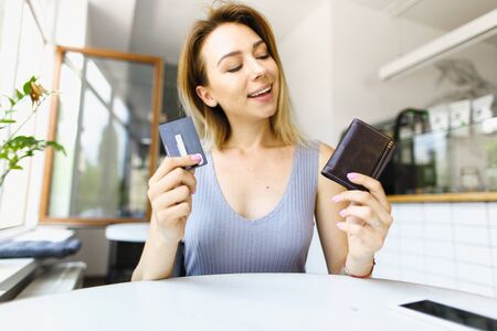 Blonde girl sitting at cafe and keeping leather wallet. Concept of paying by credit card.の写真素材
