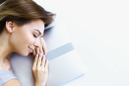 Blonde woman lying on laptop in white background with copy space. Concept of having break and preparing before exam.の写真素材