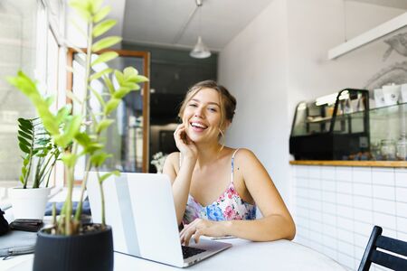 Young nice female shop assistant sitting at cafe and working with laptop. Concept of freelance job.の写真素材