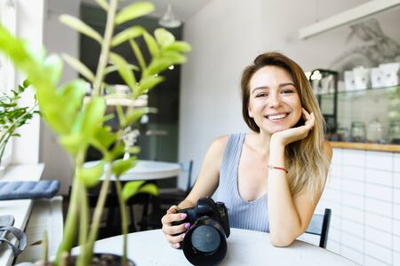 Young european female photographer sitting at cafe with camera and waiting for model. Concept of photo session at restaurant.の写真素材