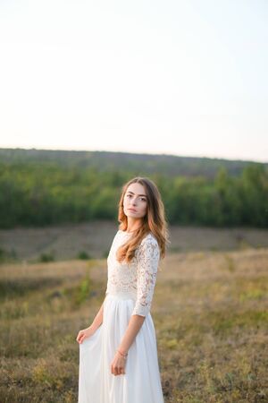 Caucasian nice fiancee standing in steppe and wearing white dress. Concept of nature, bridal photo session on nature and beauty.の写真素材