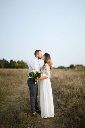 Caucasian groom kissing bride with bouquet of flowers in steppe background. Concept of happy married couple and love.の写真素材