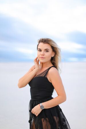 Young blonde woman wearing black transparent dress and walking on snow. Concept of vogu and seasonal photo session.の写真素材