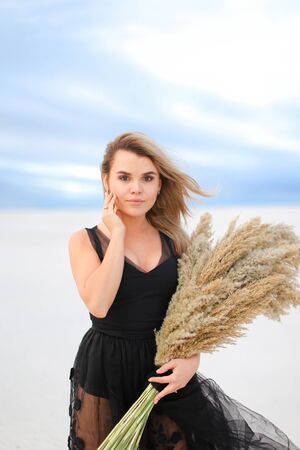 Young girl wearing black dress standing with dried plants bouquet. Concept of fashion and seasonal winter photo session.の写真素材