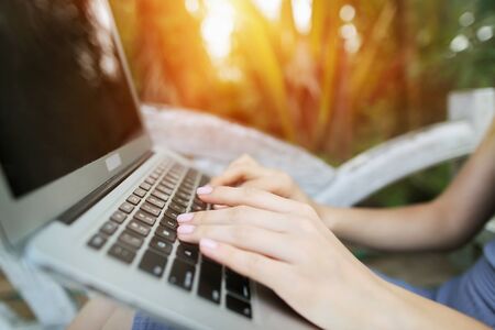 woman hand fingers press laptop keyboard for freelancing remote work on sunny day, background of sunshine green palms in Thailand, Phuket. Concept of new technologies for better life, travel to tropical countriesの写真素材