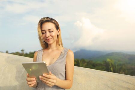 Young smiling woman using tablet with mountains background, Thailand. Concept of last minute tours, modern technology and tourism.の写真素材