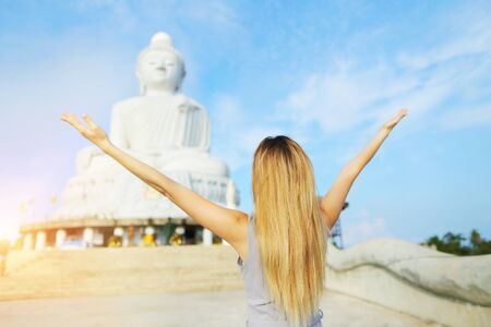 Back view of young girl with raised hands near statue of Buddha in Phuket, Thailand. Concept of tourism in Asia and famous landmarks.の写真素材