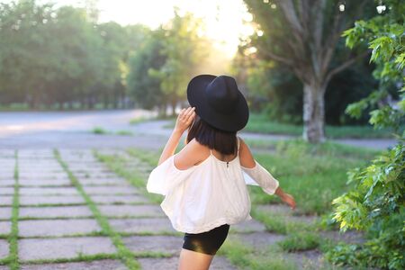 female nature keeps his hat summer sun sunset looks pleased. azitka woman black hair white shirt black shorts dancing around the trees looking at the camera. portrait. spinningの写真素材