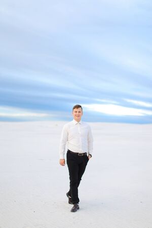 Young caucasian male person standing in winter steppe and wearing white shirt, snow in backgrounf. Concept of seasonal photo session.の写真素材