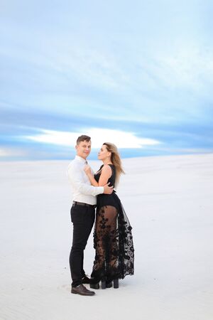 Young husband in white shirt hugging wife wearing black dress in winter steppe. Concept of winter photo session, relationship and love, happy couple.の写真素材