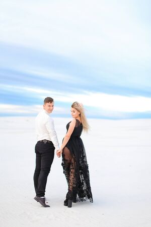 Young girl in black transparent dress holding man hands and walking in winter steppe. Concept of seasonal photo session and love.の写真素材