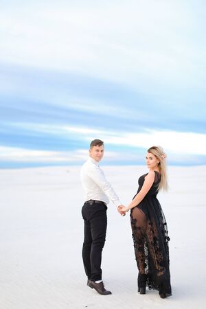 Young beautiful girl in black transparent dress holding man hands and walking in winter steppe. Concept of seasonal photo session and love.の写真素材