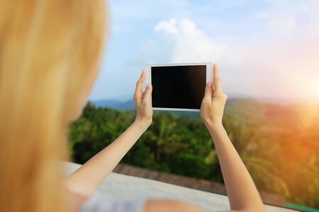 Sunshine photo of woman using tablet and taking photo of Thailand mountains. Concept of summer vacations, last minute tours and modern technology.の写真素材