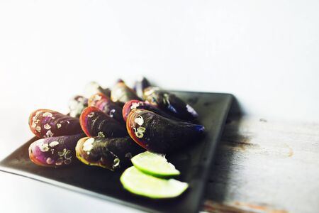 Exotic mussels and sliced lime on black square plate with lime in white background. Concept of...