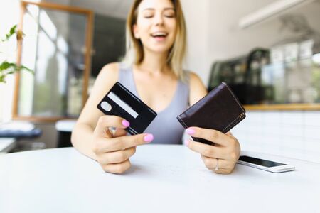 Blonde woman sitting at cafe and keeping wallet. Concept of paying by credit card.の写真素材