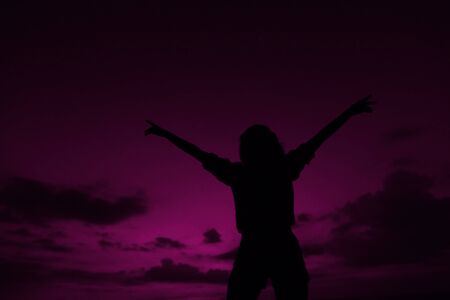 Female black silhouette with raised hands on violet sunset sky background in Hawaii. Concept of summer vacations, freedom and cheap last minute tours to southern countries.の写真素材